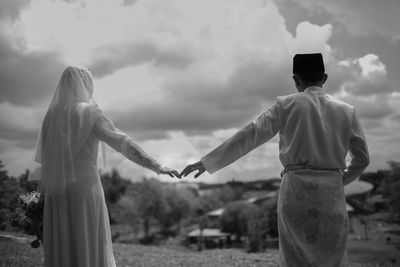 Rear view of couple standing on field against sky