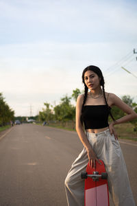 Portrait of young woman standing on road against sky