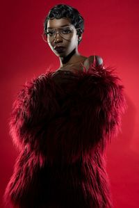 Young woman wearing eyeglasses and fur clothing standing against red background