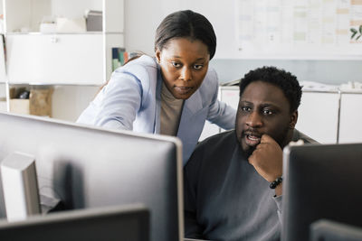 Businesswoman explaining male colleague over computer at office