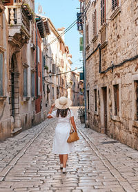 Young woman in white dress walking down the streets of picturesque old town in summer.