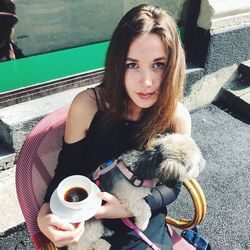 High angle portrait of woman with dog sitting on chair at sidewalk cafe