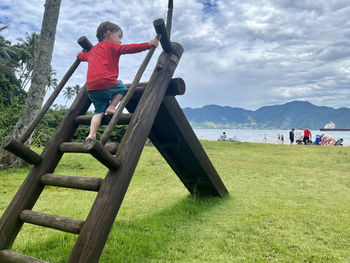 Child in a red blouse climbing the stairs of a slide in a park on the beach