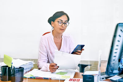 Middle-aged woman social worker check accounts bills, using smartphone to communicate. 