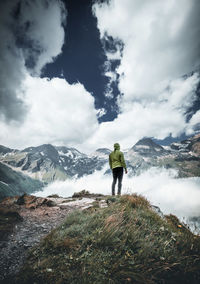 Rear view of man standing on snowcapped mountain against sky