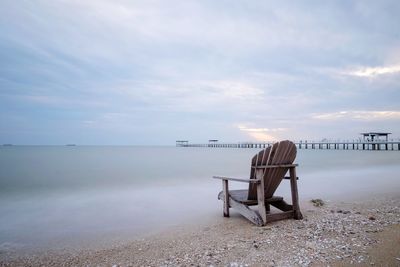 Empty bench on beach against sky