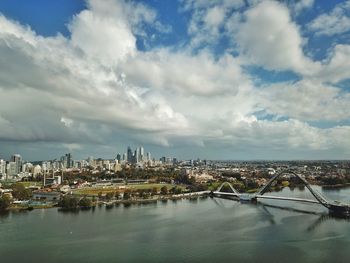 Bridge over river by buildings in city against sky