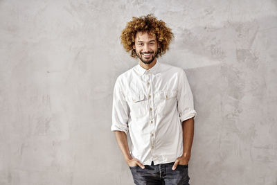 Portrait of smiling young man standing at grey wall