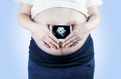 Midsection of woman holding camera while standing against white background