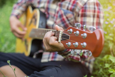 Midsection of man playing guitar while sitting on grass