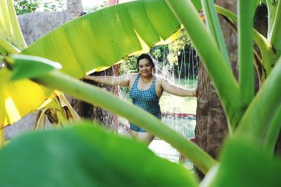 Portrait of smiling woman seen through plants standing under shower