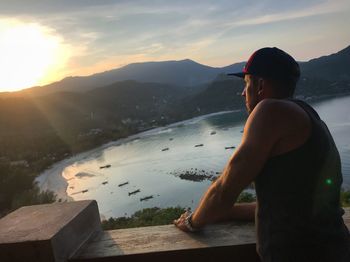 Rear view of shirtless man standing by sea against sky during sunset