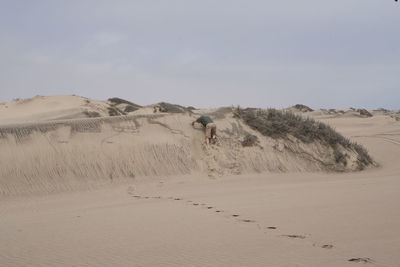 Full length of man climbing on sand dune at desert against sky