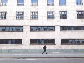 Side view of man walking on footpath against building in city