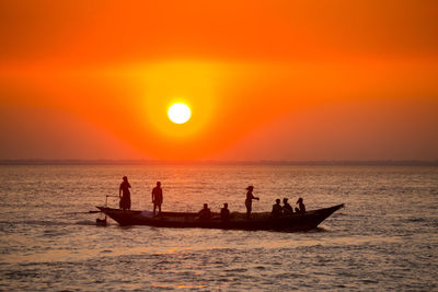 Silhouette people in sea against sky during sunset