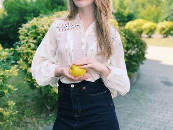 Midsection of young woman holding apple while standing outdoors