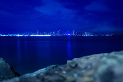 Illuminated city by sea against sky at night