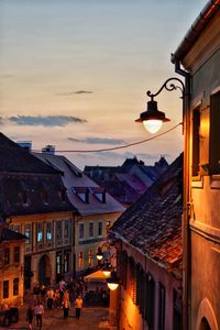 Illuminated street amidst buildings against sky at sunset