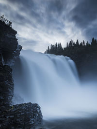 Tannforsen waterfall flowing by rocks and trees against sky