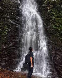 Rear view of woman looking at waterfall in forest