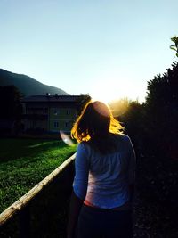 Rear view of woman standing on field against sky during sunset