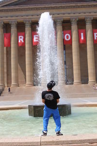 Optical illusion of man rising fountain by urinating against historic building