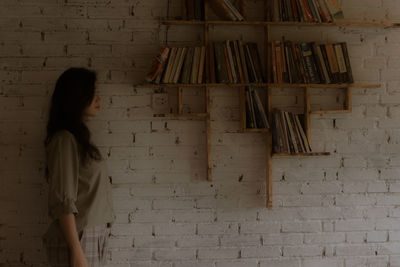 Side view of woman standing against brick wall