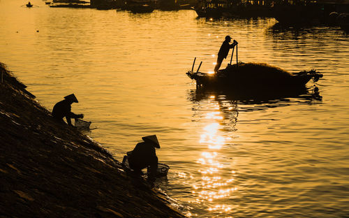 Silhouette people fishing in lake during sunset