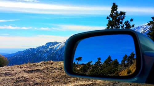 Reflection of trees on side-view mirror against blue sky