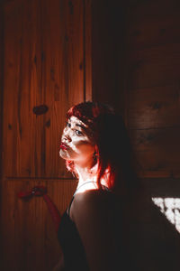 Sunlight falling on young woman standing by wall at home