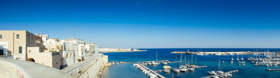 Boats moored at harbor against clear blue sky