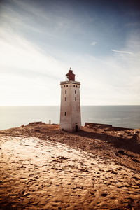 Lighthouse on beach by sea against sky