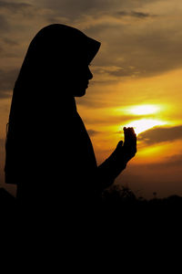 Silhouette woman holding orange while standing against sky during sunset