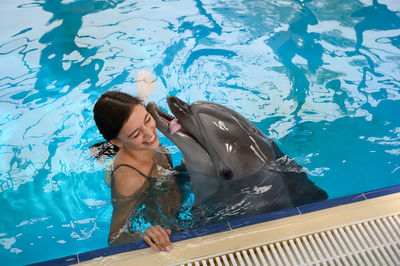 High angle view of smiling young woman with dolphin swimming in pool