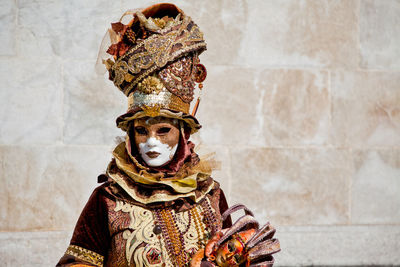 Woman in costume and mask during carnival standing against wall