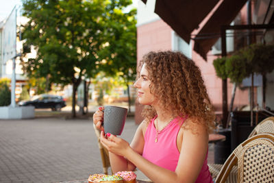 Young attractive curly woman sits at table in cafe on summer terrace. colorful 