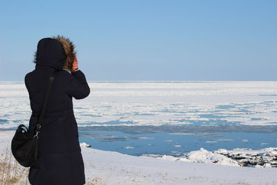 Rear view of woman looking at frozen lake against clear blue sky