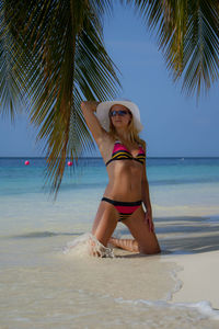 Sensuous young woman in bikini kneeling on shore at beach