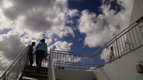 Low angle view of people walking on steps against cloudy sky