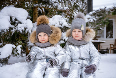 Little brother and sister on winter walk in park in winter overalls sit in snow