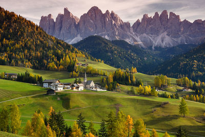 Scenic view of field by houses and mountains against sky