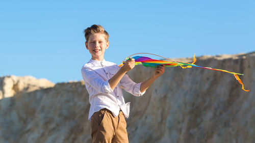 A boy in white shirt with a kite in his hands plays in the mountains.