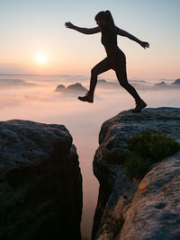 Silhouette man jumping on rock against sky during sunset