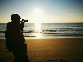 Man drinking drink at beach against sky