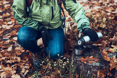 Woman with backpack having break during autumn trip on autumn cold day pouring a hot drink