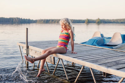 Girl sitting on pier over lake against sky