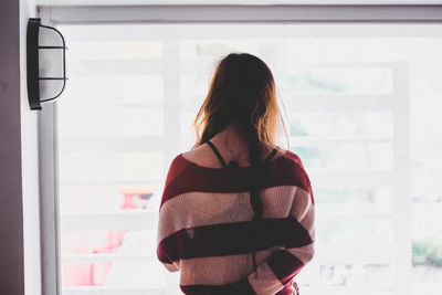 Rear view of woman standing by glass window at home