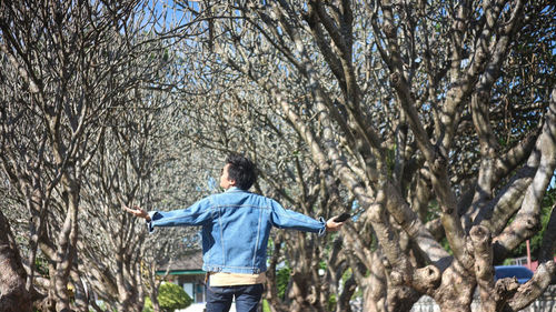 Rear view of woman with arms outstretched standing amidst bare trees in forest