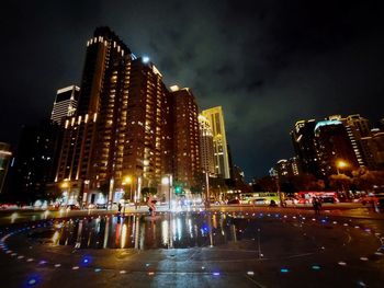 Illuminated buildings by street against sky at night