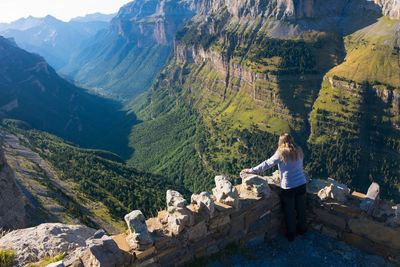 One woman from behind at an ordesa national park balcony admiring from the top of the mountain the whole valley, the green forests, the rocks, the hills and the horizon. horizontal photo